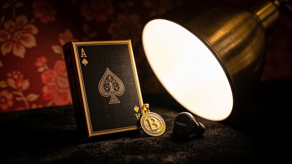 A boxed deck of black playing cards, a gold pin and a small haptic device